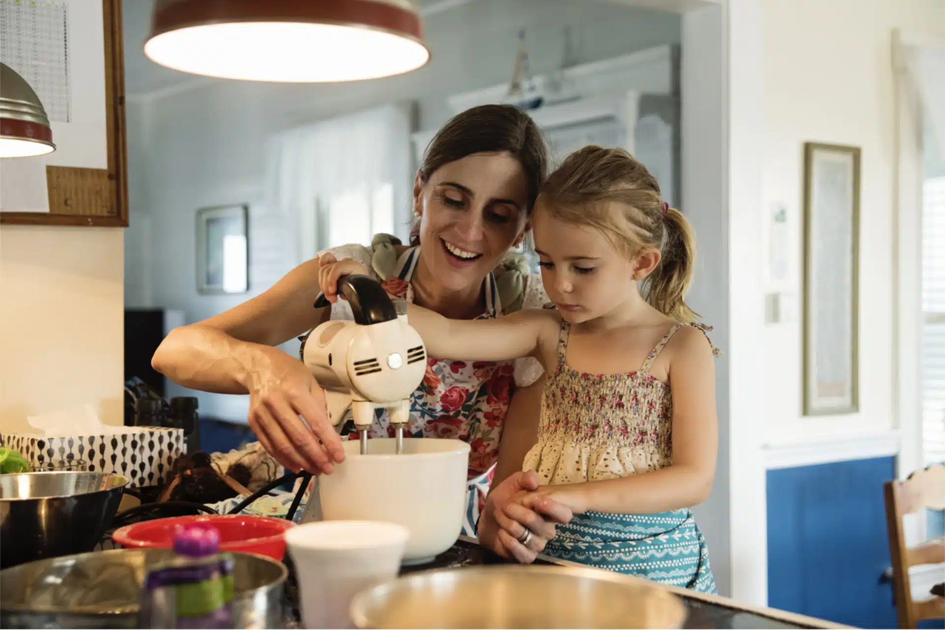 Mother and young daughter mixing cake batter with an electric mixer.